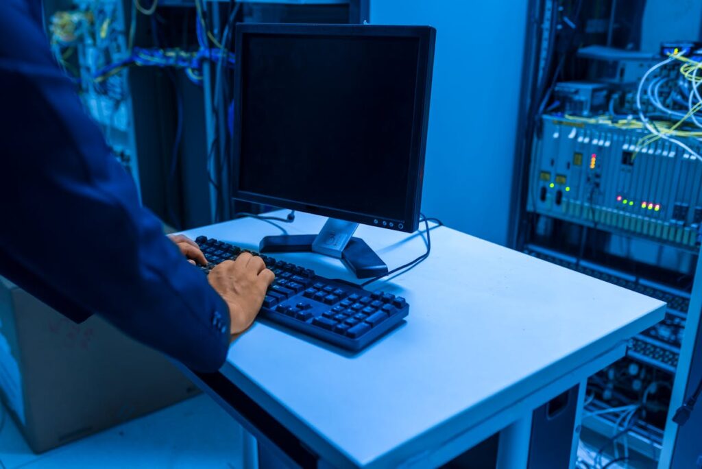 A person types on a computer in a dark room with machines.