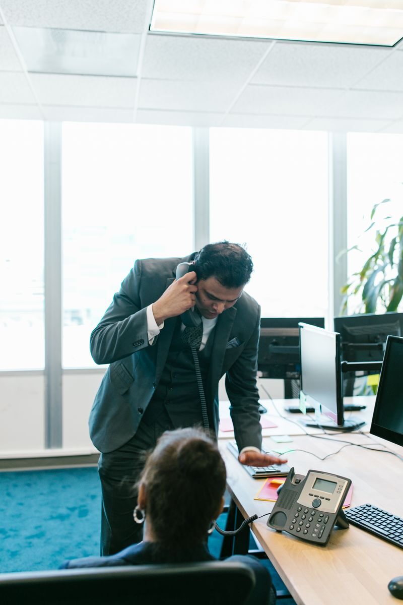 Professional communicating on phone in a contemporary office setting, discussing work with a colleague.