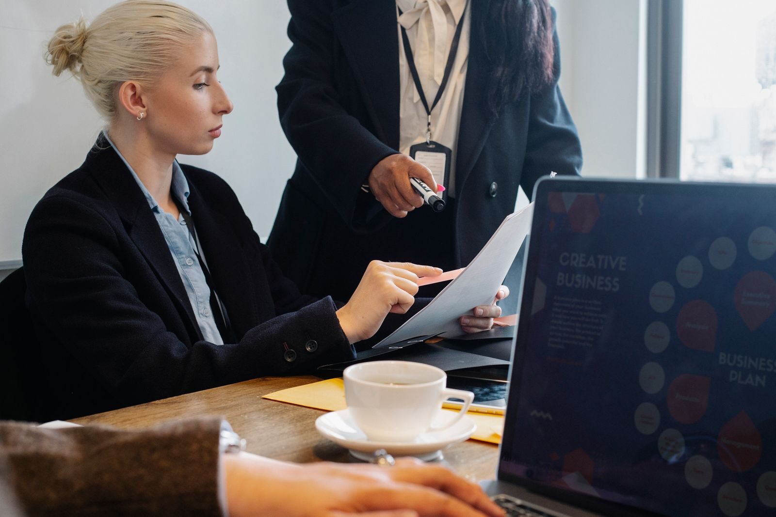 Group of coworkers in formal wear gathering at table and discussing details of business plan in modern workspace